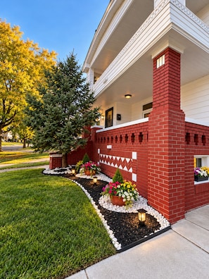 A house with a red brick exterior, a white porch, and a landscaped garden with flower beds. - Just Minutes From Downtown, Cleveland Clinic & University Circle, Free Parking (Cleveland)
