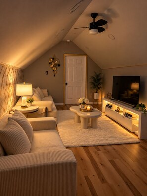 Ein modernes Wohnzimmer mit hohen Decken, einem Deckenventilator, einem Flachbildfernseher, einer Couch, einem Couchtisch und einem Wanddekor.