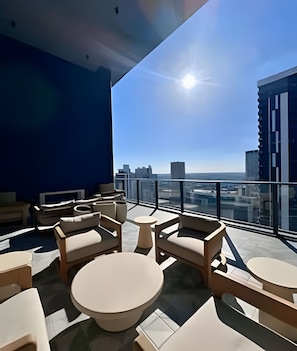 Un moderno salón en la azotea con vistas a la ciudad, que cuenta con mobiliario contemporáneo y barandilla de cristal.