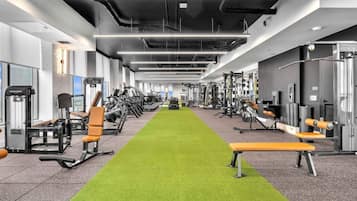 Ein Fitnessraum mit verschiedenen Trainingsgeräten, einem grünen Rasenlaufweg und Bänken.