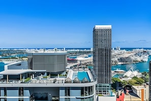 Um edifício moderno e imponente, com design angular característico, localizado em uma paisagem urbana costeira com um porto de iates e uma grande roda-gigante ao fundo.