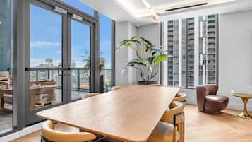 A modern interior with a large wooden table, comfortable seating, a potted plant, and a view of the city through large windows.