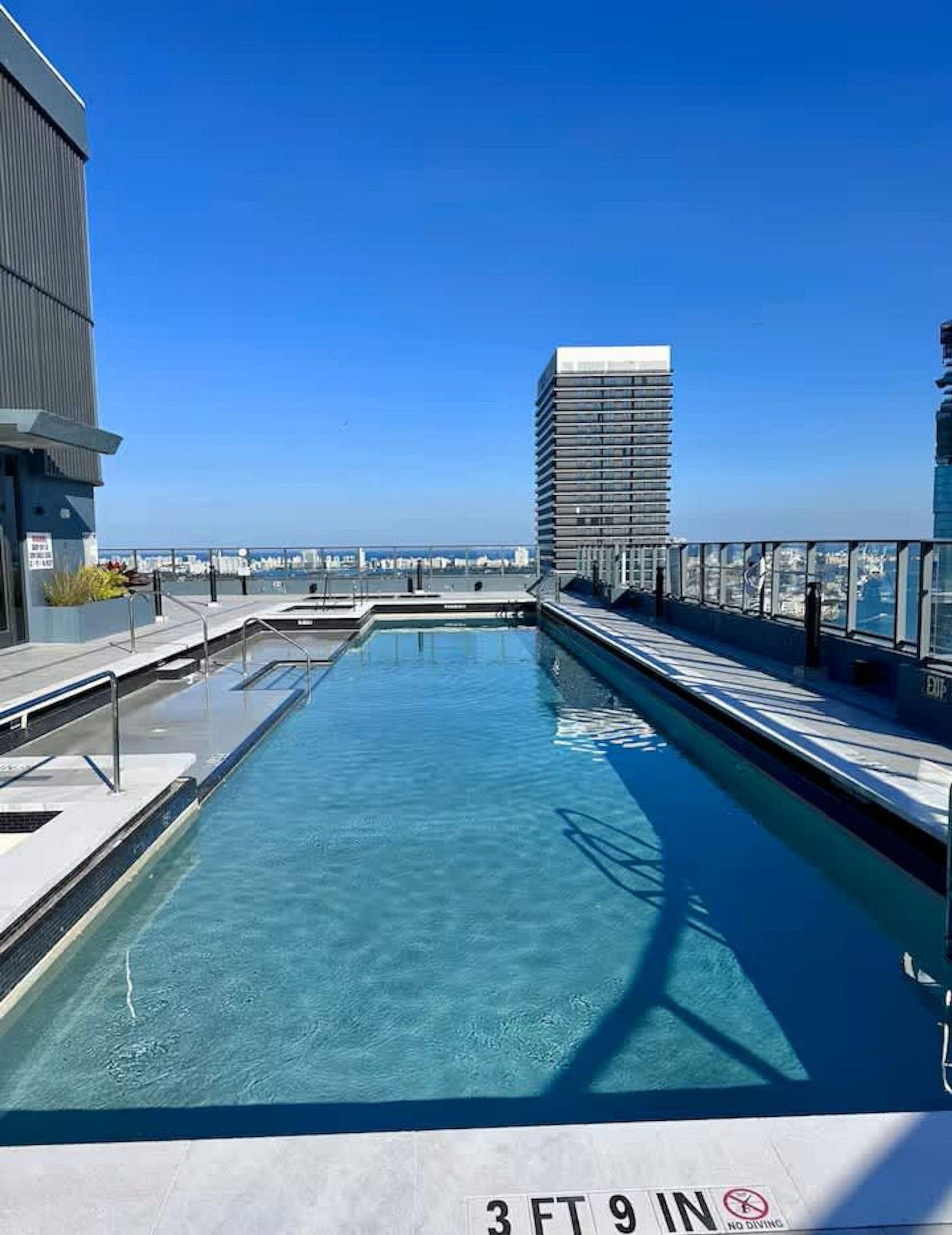Una piscina en la azotea con agua azul cristalina, rodeada de edificios modernos y un cielo despejado.