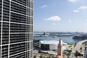 A high-rise building with multiple floors and balconies, overlooking a waterfront area with a large circular structure and a bridge. - 501 First - Rooftop Pool - Gym (Miami)