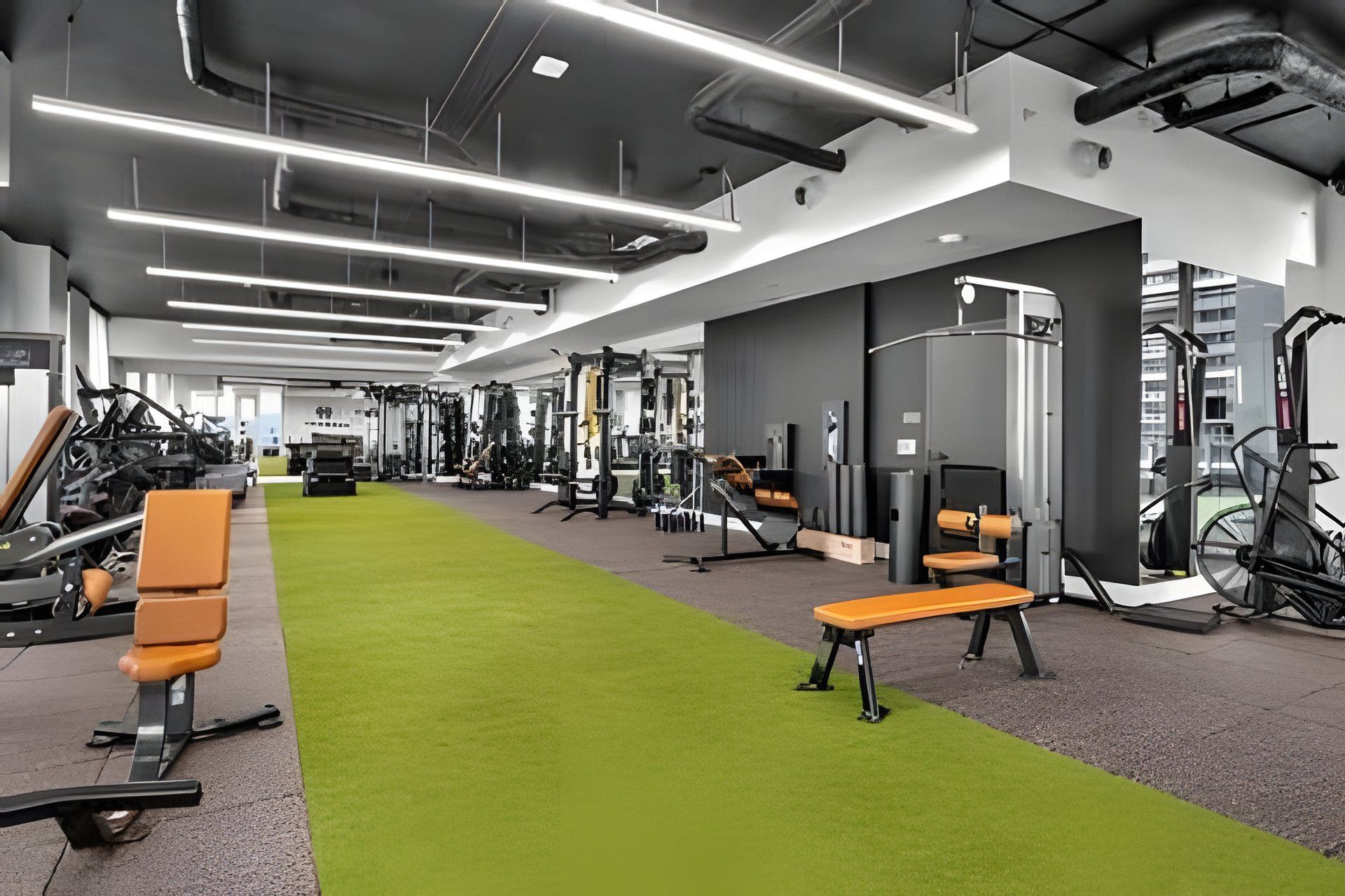 A modern gym with various exercise equipment, a green carpet, and benches.