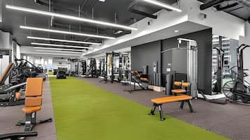 A modern gym with various exercise equipment, a green carpet, and benches.