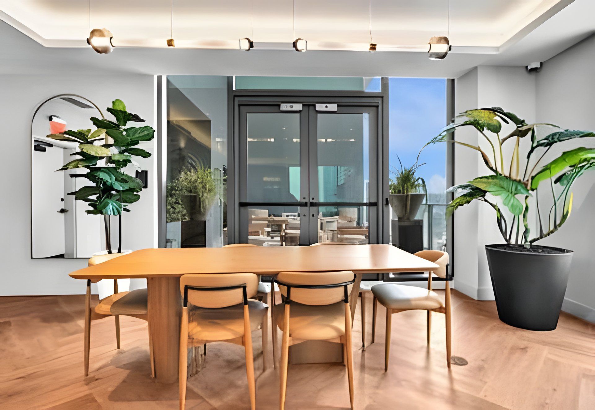 Uma sala de jantar moderna com mesa e cadeiras de madeira, janelas amplas e plantas em vasos.