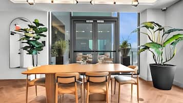 Uma sala de jantar moderna com mesa e cadeiras de madeira, janelas amplas e plantas em vasos.