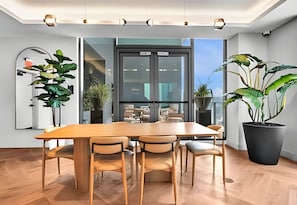 Uma sala de jantar moderna com mesa e cadeiras de madeira, janelas amplas e plantas em vasos.