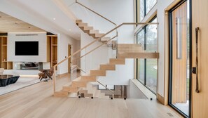 A modern interior with a staircase, a flat-screen TV, and a large window. - Brand new 2026 designer construction- Full privacy-Gym-Sauna-Hotel bar- Firepit. (East Hampton)