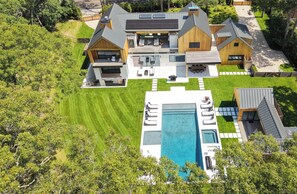 A modern house with a large swimming pool, multiple outdoor seating areas, and a well-maintained lawn. - Brand new 2026 designer construction- Full privacy-Gym-Sauna-Hotel bar- Firepit. (East Hampton)