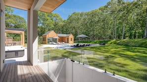 Une terrasse extérieure moderne avec des garde-corps en verre, un espace piscine avec des chaises longues et une structure de cabane en bois.