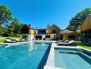 Et moderne hus med swimmingpool, liggestole og en overdækket patio.