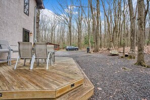Eine Holzterrasse mit Stühlen, eine kleine Holzhütte und ein Kiesweg, der zu einem Parkplatz führt.