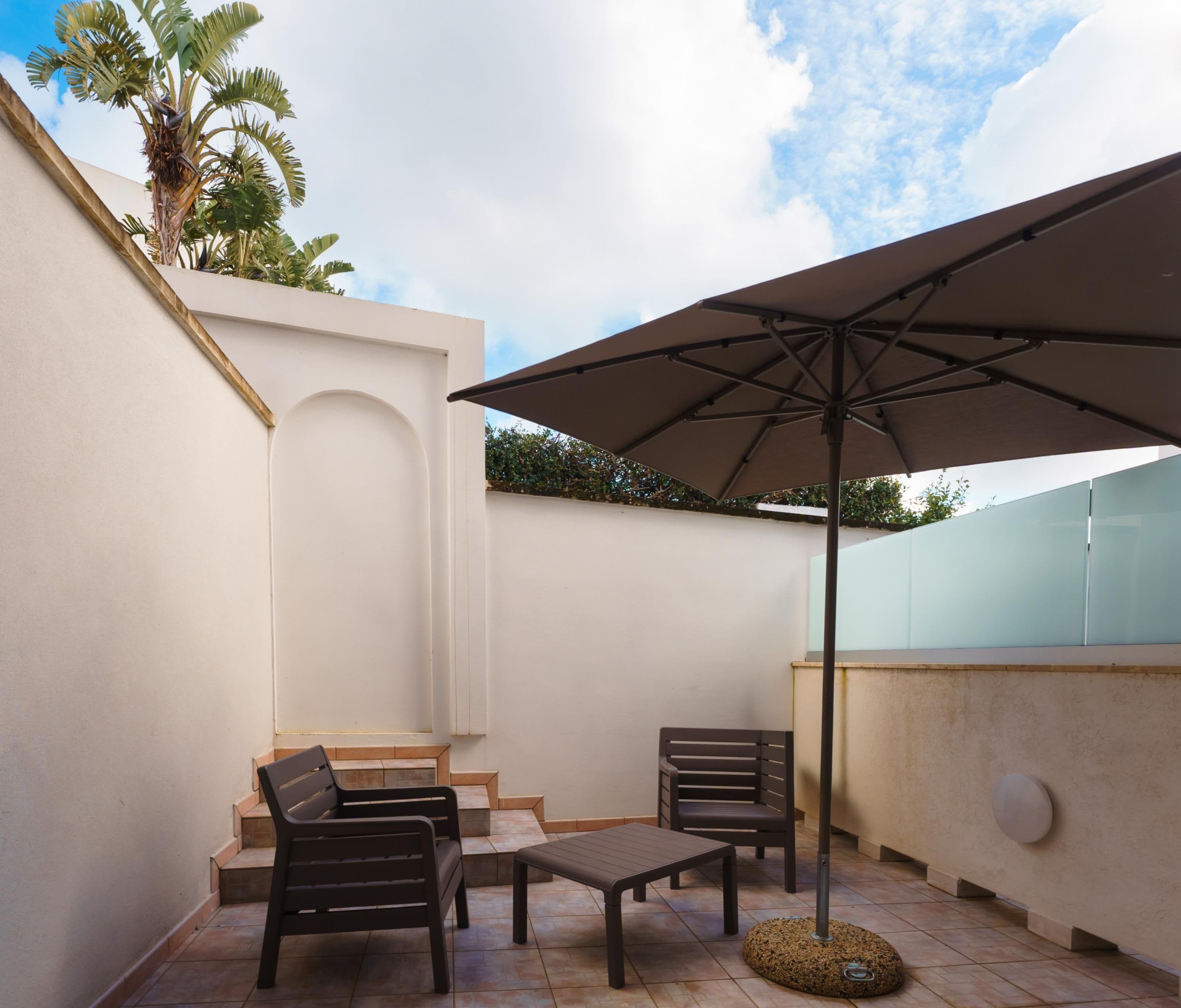 A patio with two chairs, a small table, and a large umbrella.