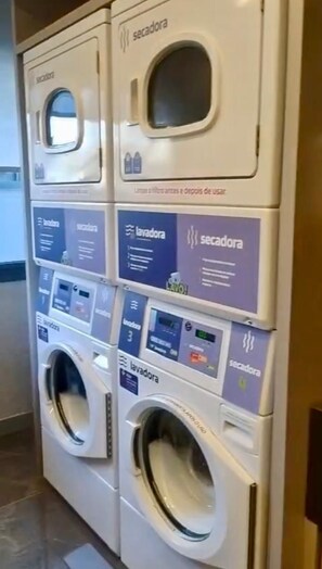 Une rangée de machines à laver, dotées de panneaux de commande, dont certaines sont étiquetées « sécheuse » et d’autres « lave-linge ».