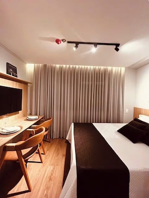 Ein Hotelzimmer mit Bett, Schreibtisch mit Stuhl, Flachbildfernseher und Deckenventilator.