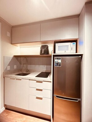 Eine kompakte Küche mit einer eingebauten Mikrowelle, einem Edelstahlkühlschrank und einem Spülbecken mit Armatur.