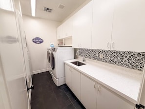 A laundry room with a washing machine, a sink, and a tiled backsplash. - Pool & Hot Tub / 4 BR 4 BA / Outdoor Living (Tucson)