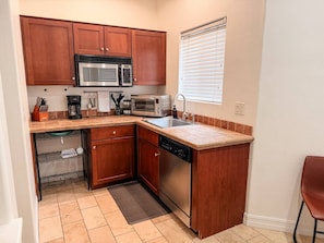 A compact kitchen with wooden cabinets, a stainless steel dishwasher, a microwave, and a toaster.