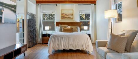 A bedroom with a bed, bedside tables, a sofa, a TV, and a large window with curtains.