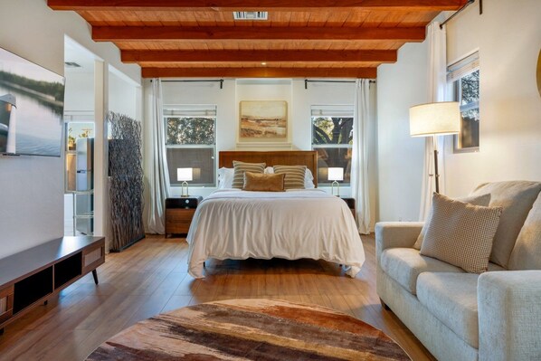 A bedroom with a bed, bedside tables, a sofa, a TV, and a large window with curtains.