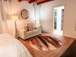 A bedroom with a bed, a sofa, a round rug, a lamp, a mirror, and a door leading to a bathroom.