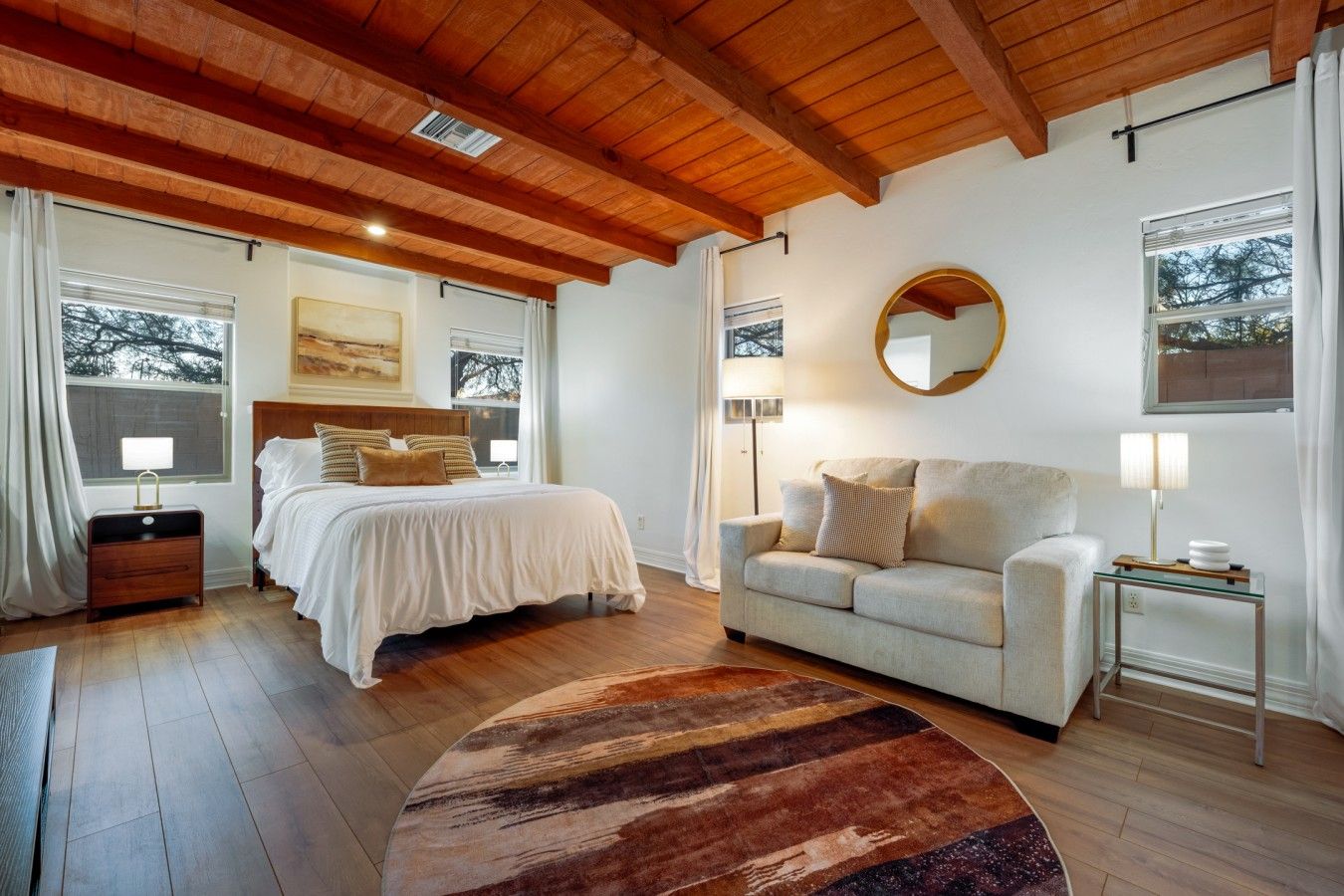 Een slaapkamer met een bed, een bank, een rond tapijt en een spiegel aan de muur.