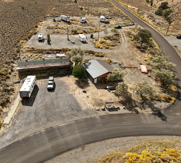 An RV park with multiple RVs parked, a building with a sloped roof, and a paved road curving through the area.