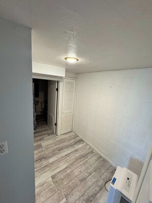 A room with a white brick wall, a wooden floor, and a ceiling light.