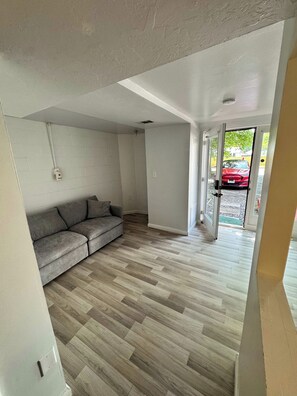 A room with a grey sofa, wooden flooring, and a door leading outside.