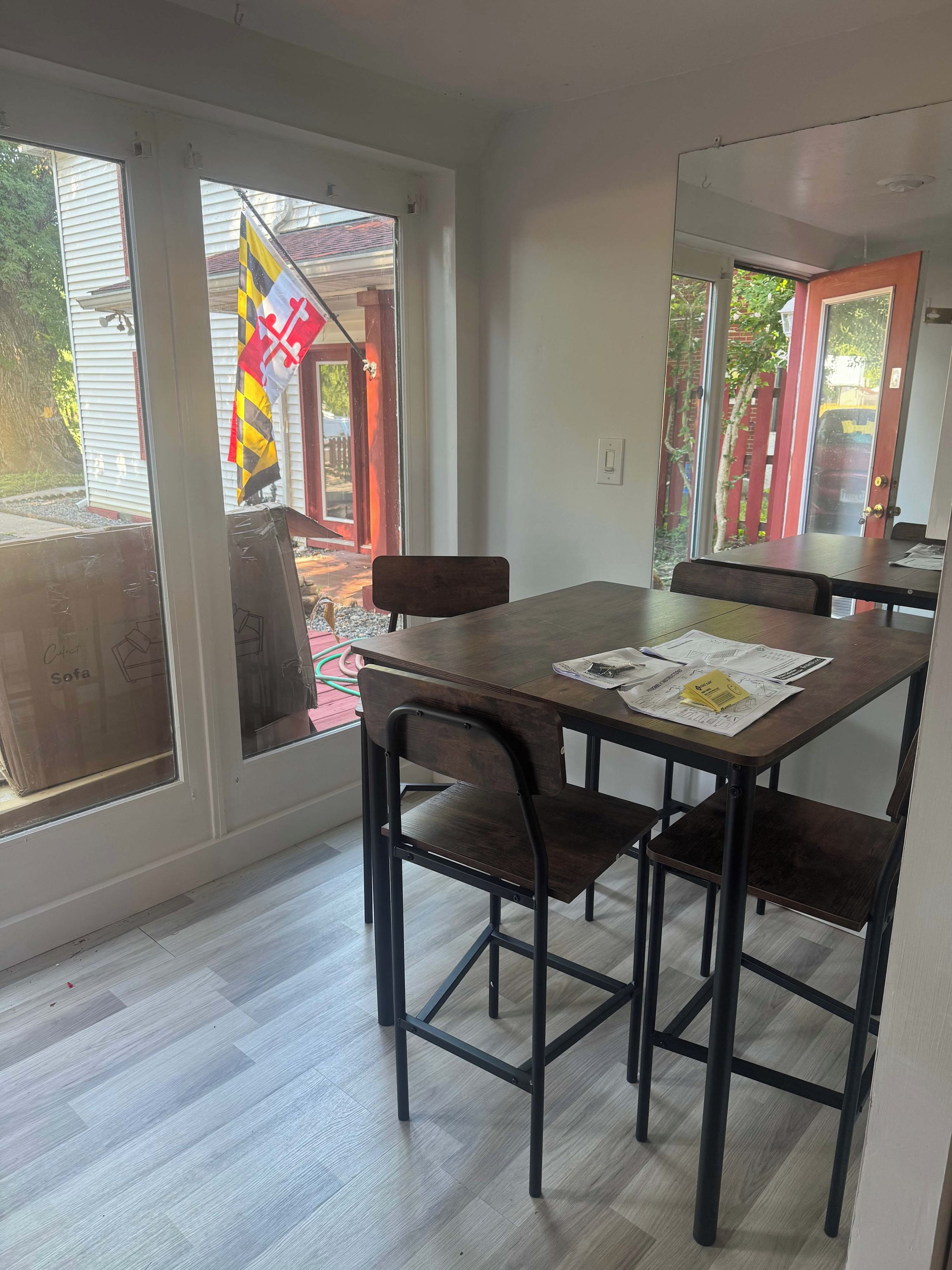 A dining area with a table and chairs, a window with a view of the outside, and a door with a red frame.