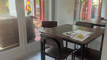 A dining area with a table and chairs, a window with a view of the outside, and a door with a red frame.