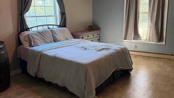 A bedroom with a bed, a dresser, a window with curtains, a ceiling fan, and a tiled floor.