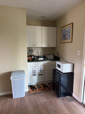 A compact kitchen with white cabinets, a microwave, and a small refrigerator.