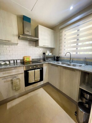 A modern kitchen with white cabinets, a stainless steel sink, and a built-in oven. - Luxury Apartment in Punta Cana: View from the Poll (Punta Cana)