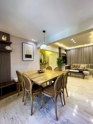 A dining area with a wooden table and chairs, a hanging light fixture, and a view into the living room. - Luxury Apartment in Punta Cana: View from the Poll (Punta Cana)