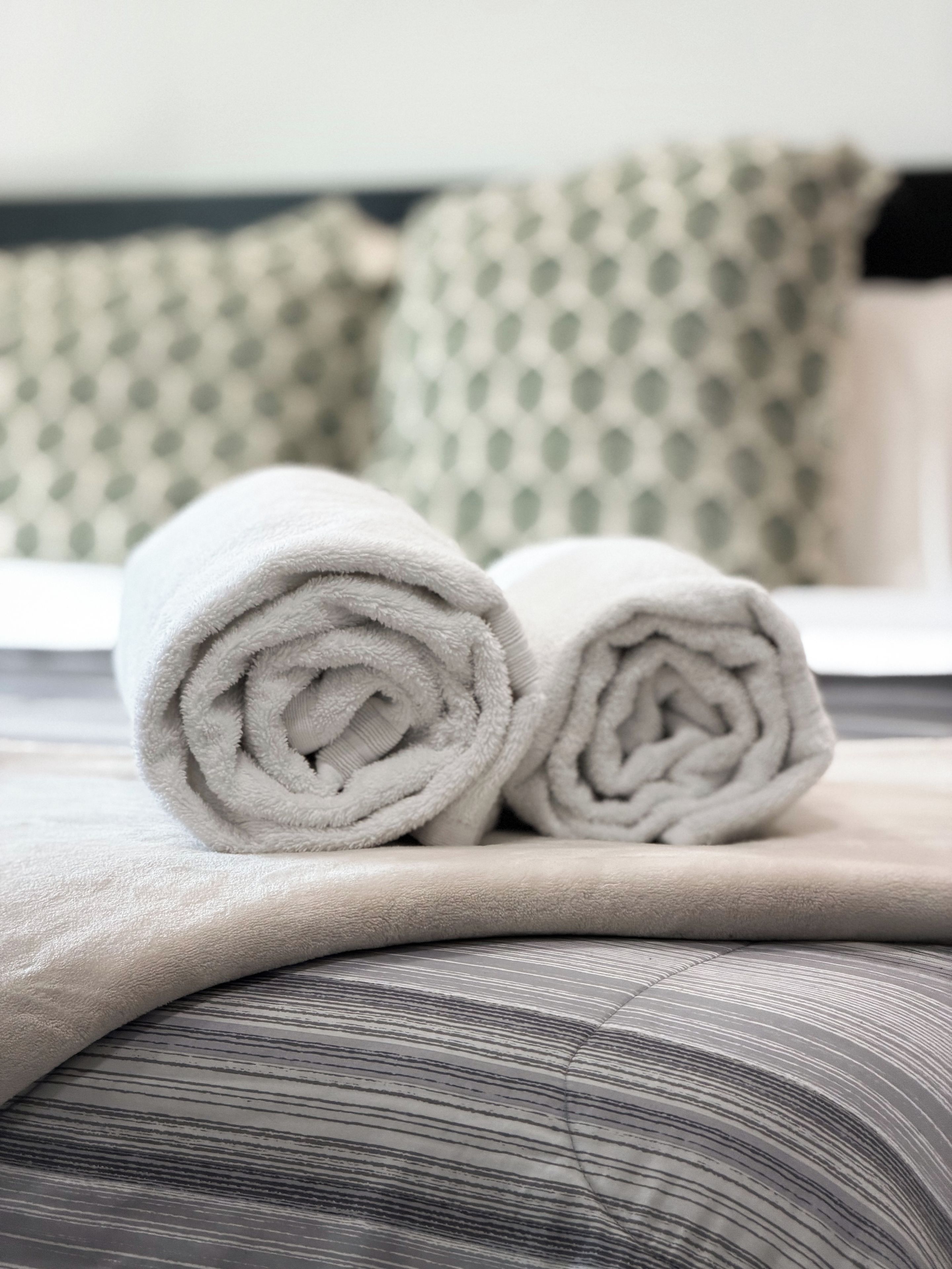 A neatly made bed with rolled white towels and a striped pillow.