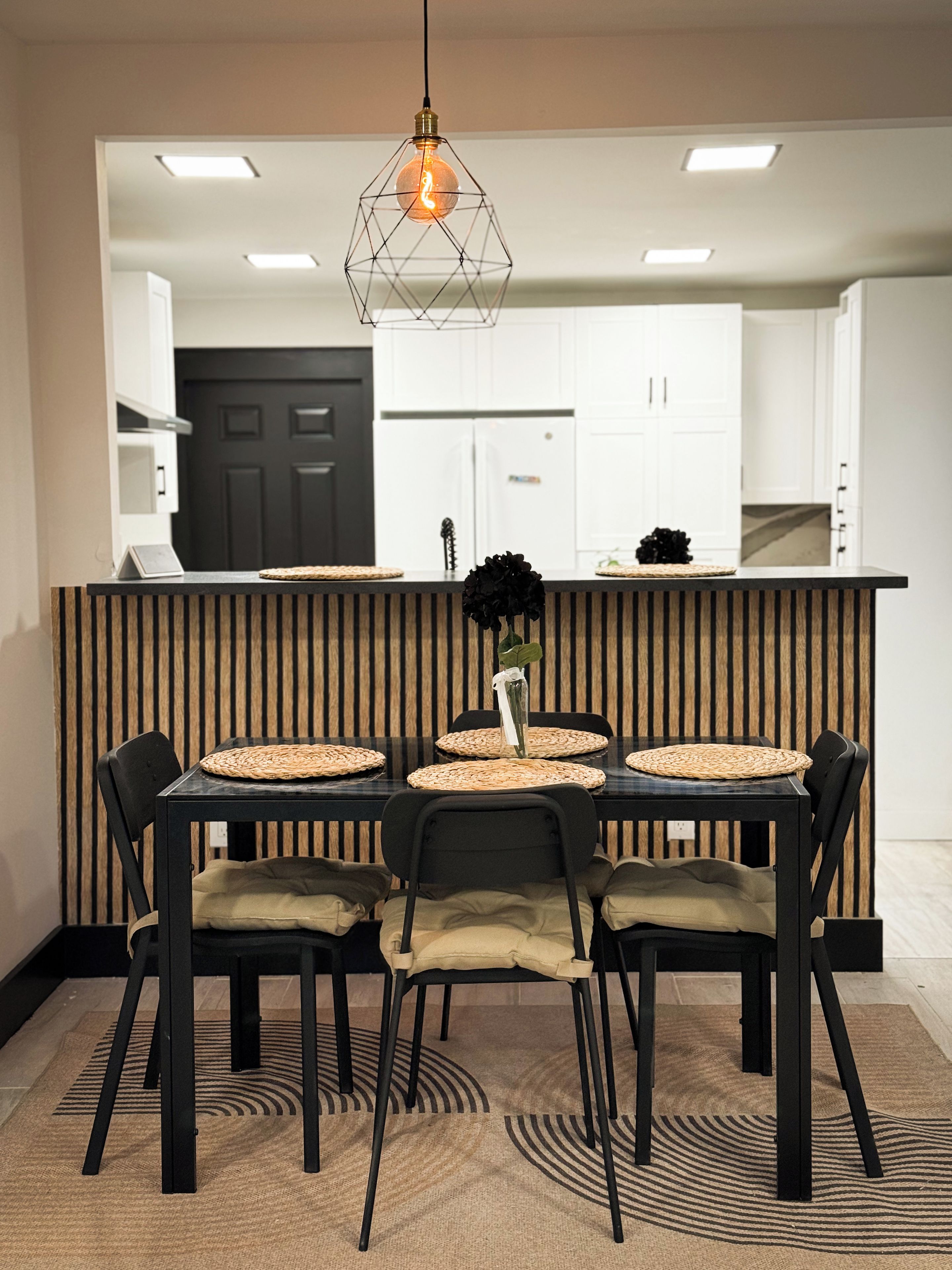 A modern kitchen with a central island, black chairs, and a hanging light fixture.