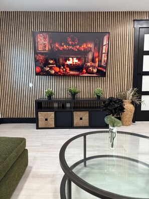 A modern living room with a flat-screen TV mounted on a wooden wall, a glass coffee table, and a green sofa. - Near Downtown Pickleball Paradise (Naples)