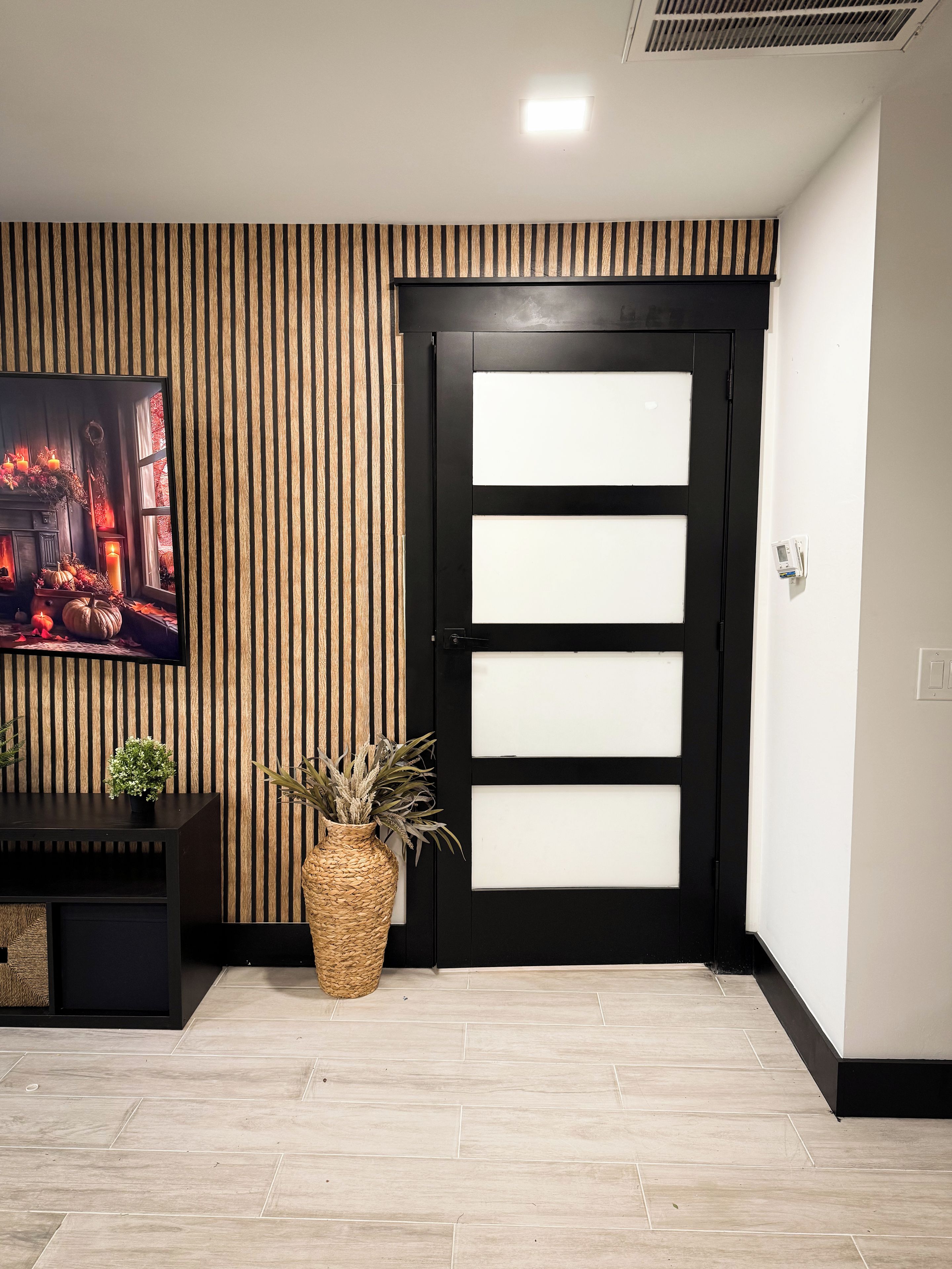 A modern interior with a black-framed door, a flat-screen TV on the wall, and a woven basket on the floor.