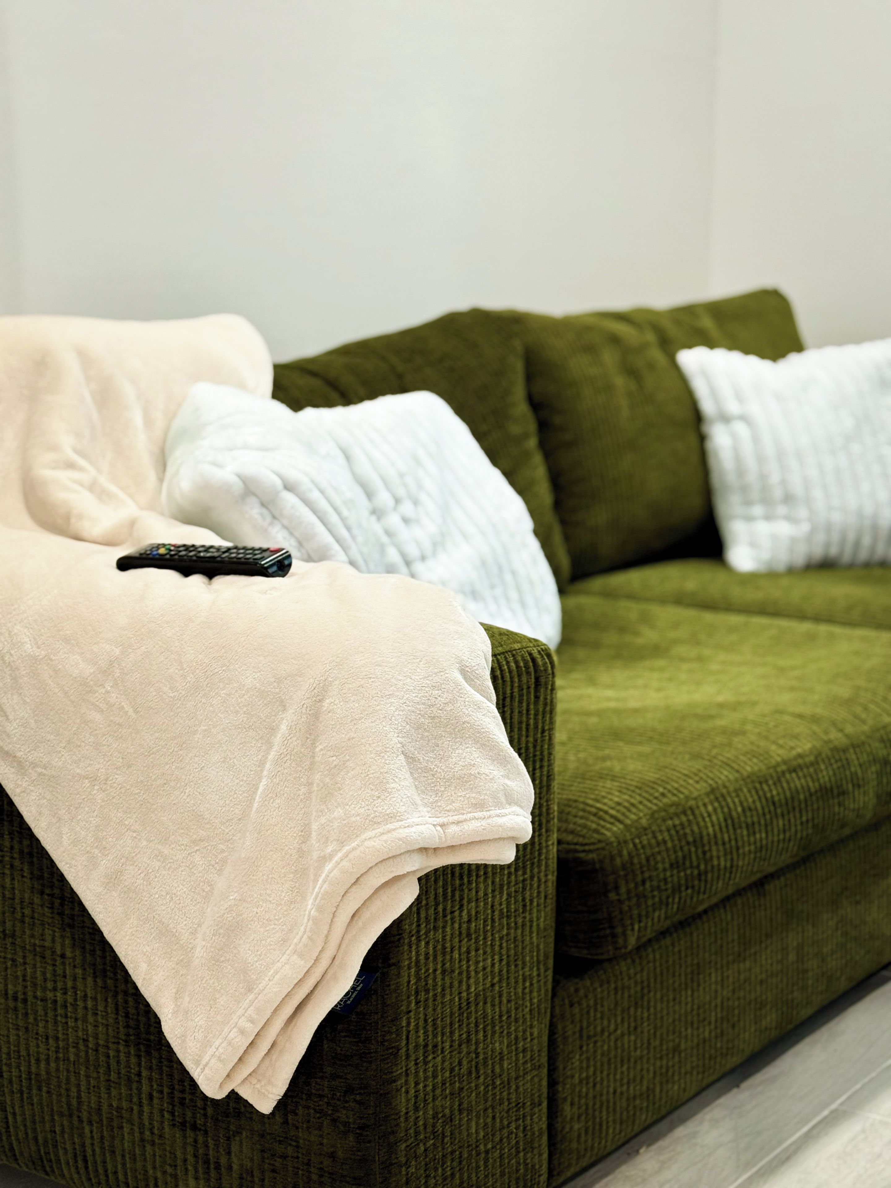 A green sofa with a white and a beige blanket, and a remote control on it.