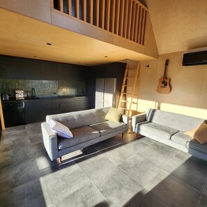 A modern living space with a sofa, a second seating area, a kitchen, and a guitar. - Surf & Fish Beach Retreat (Whangamatā)