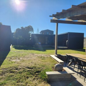 A backyard with a pergola, a barbecue area, and a grassy lawn. - Surf & Fish Beach Retreat (Whangamatā)
