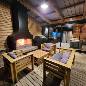 An outdoor seating area with wooden furniture and a wood-burning stove. - Surf & Fish Beach Retreat (Whangamatā)