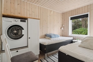 A compact bedroom with a washing machine, a bed, a bedside table, and a window with a view of greenery. - Holiday home near the beach on Rømø (Rømø)