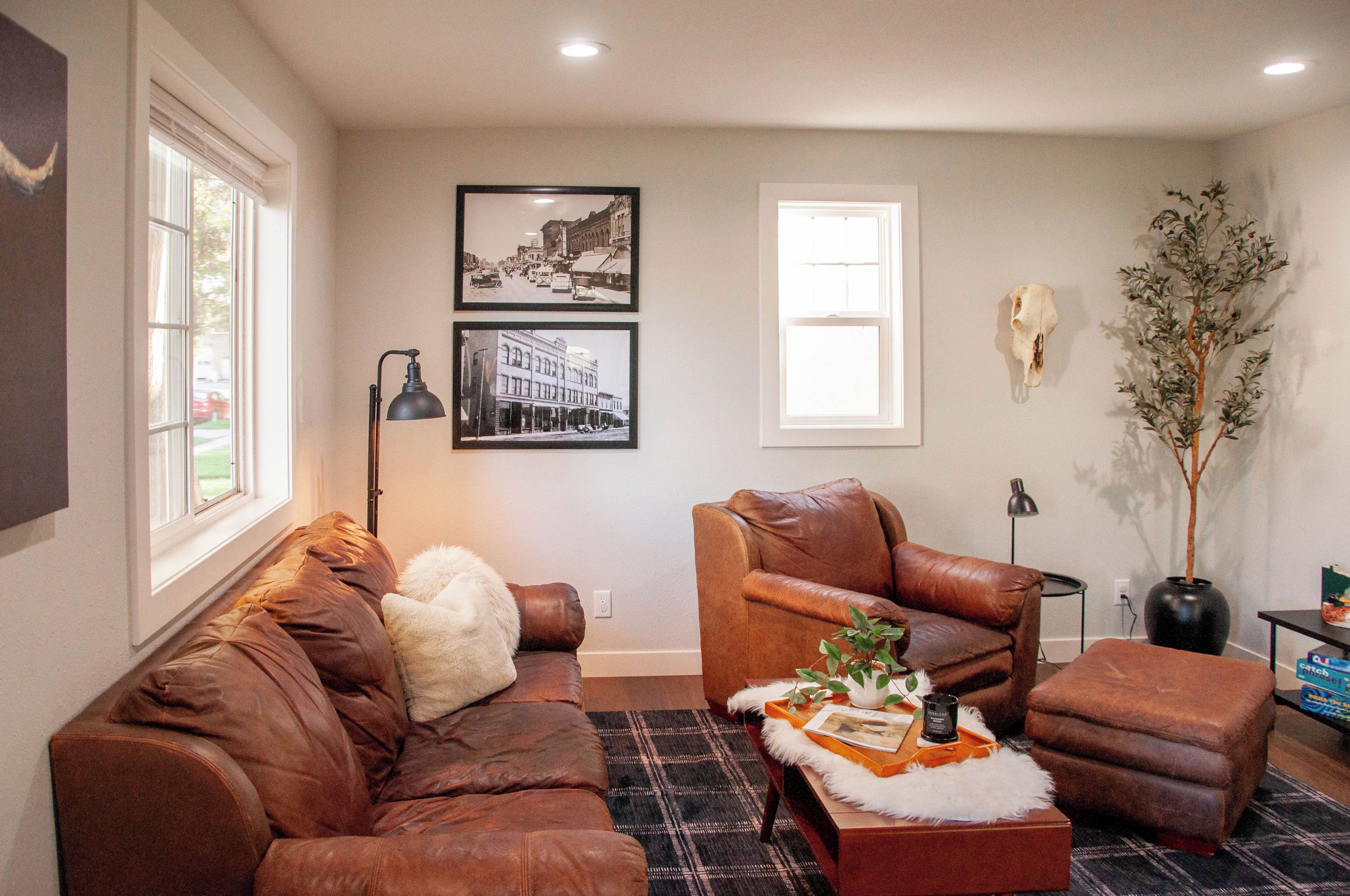 A living room with a brown leather sofa, a brown leather armchair, a small table with a tray, and a potted plant.