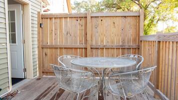 A wooden deck with a metal table and chairs, a wooden fence, and a house in the background.