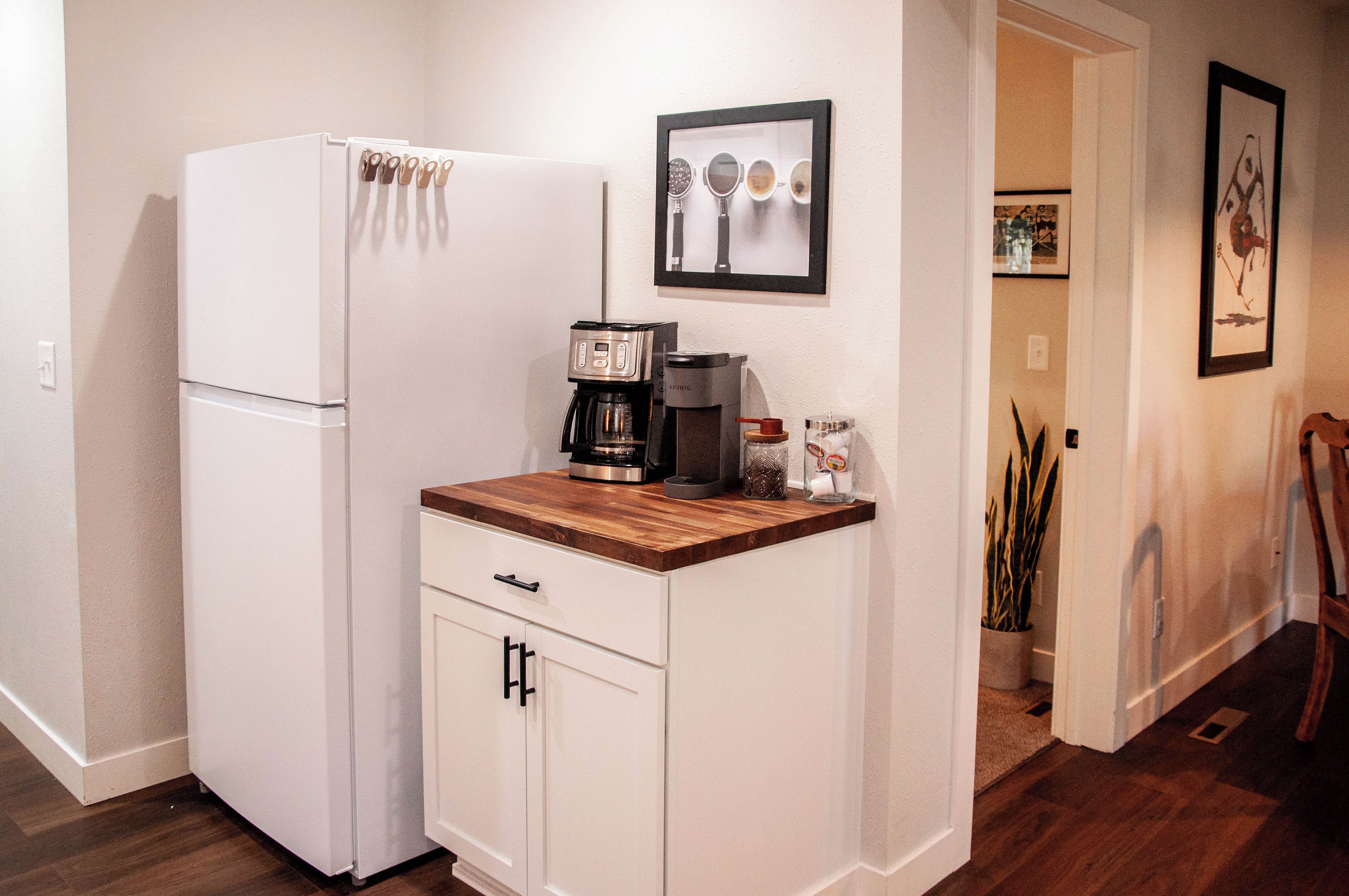 A compact kitchenette with a refrigerator, a coffee maker, and a small cabinet.