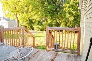 Une terrasse en bois avec une table et des chaises en métal, entourée d’une clôture en bois et d’arbres.